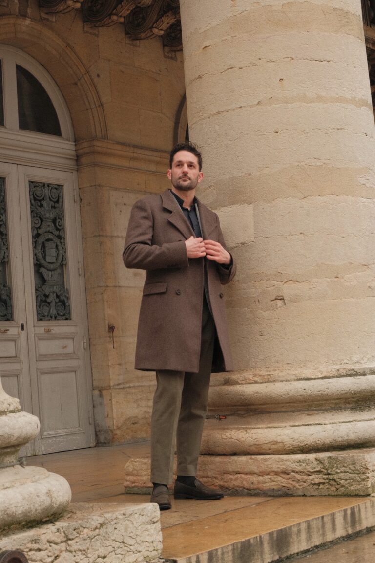 Manteau sur mesure brun porté devant les colonnes d’un bâtiment dijonnais, Auguste Tailleur